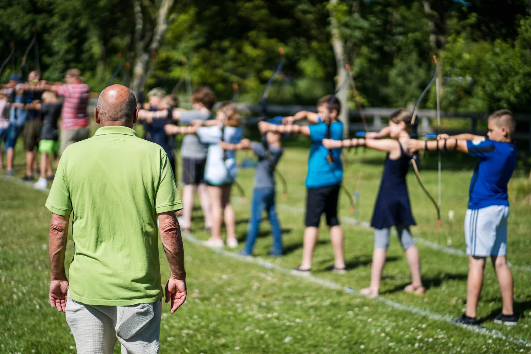 Kinder und Erwachsene in einer Reihe beim Bogenschießen auf der Wiese
