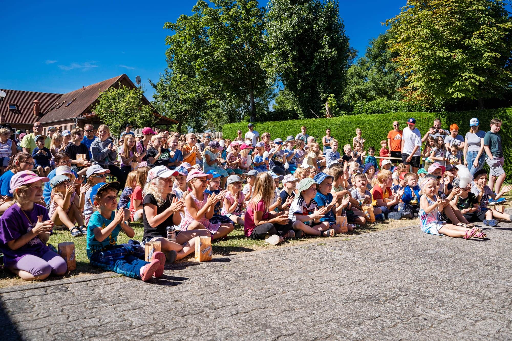 Viele Kinder sitzen beim Animationsprogramm auf der Wiese vor der Bühne