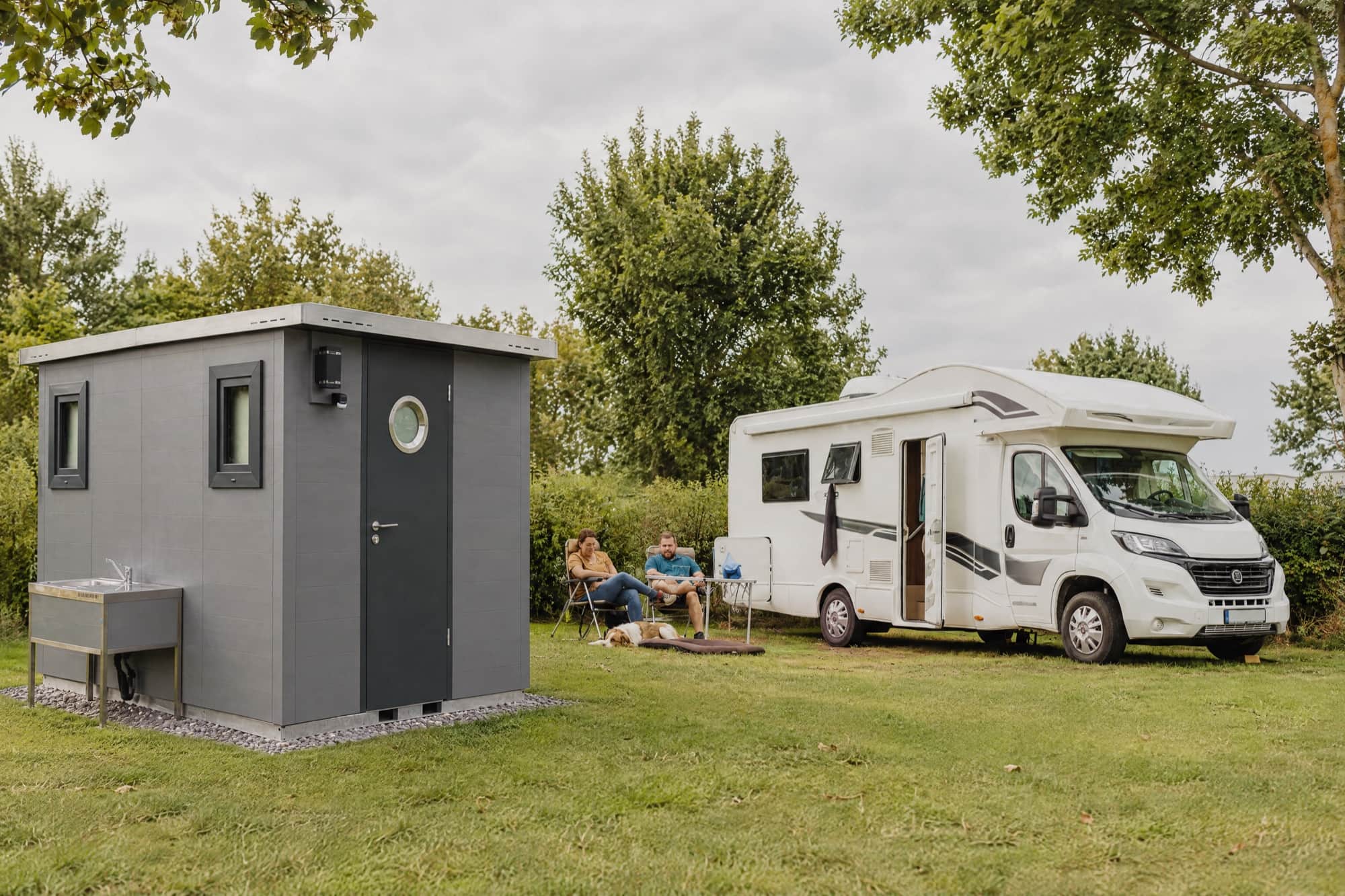 Stellplatz mit Wohnmobil und eigener grauer Sanitärkabine auf der Wiese