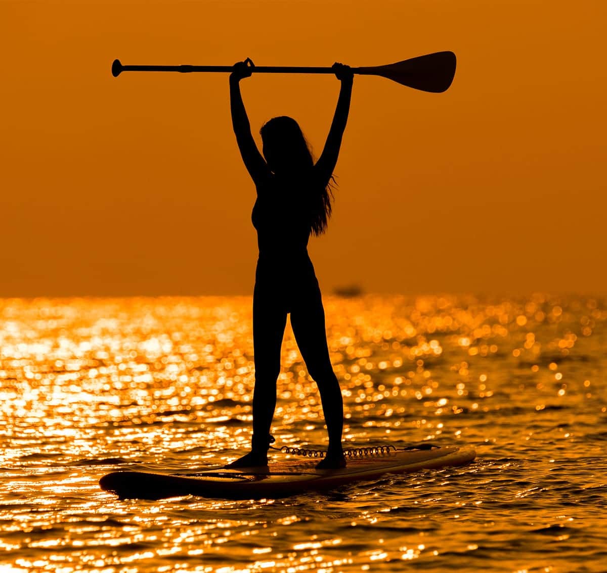 Stand-Up-Paddlerin im Gegenlicht des Sonnenuntergangs