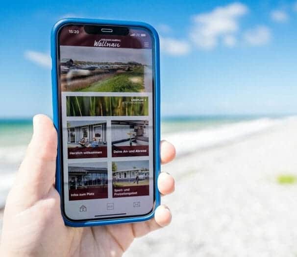 Hand hält ein Telefon mit der Strandcamping-App am Strand
