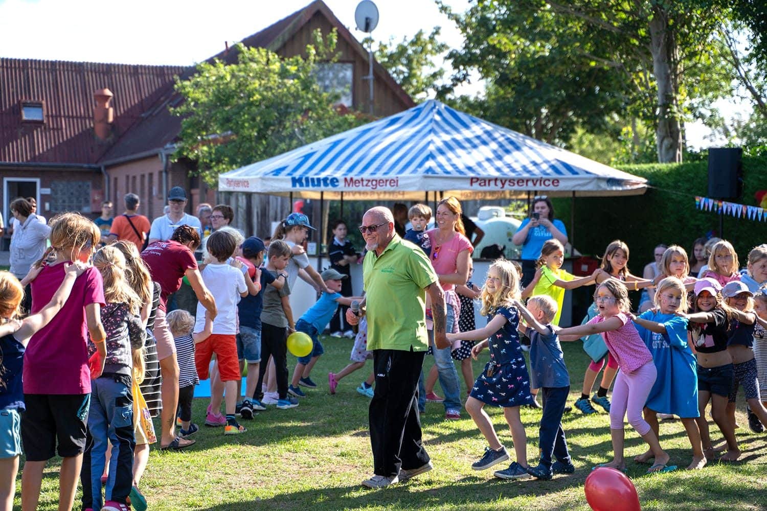 Animateur tanzt mit Kindern beim Sommerfest auf der Wiese