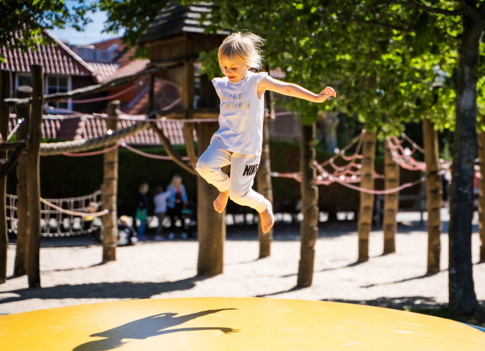 Kind springt hoch über dem gelben Hüpfkissen am Spielplatz