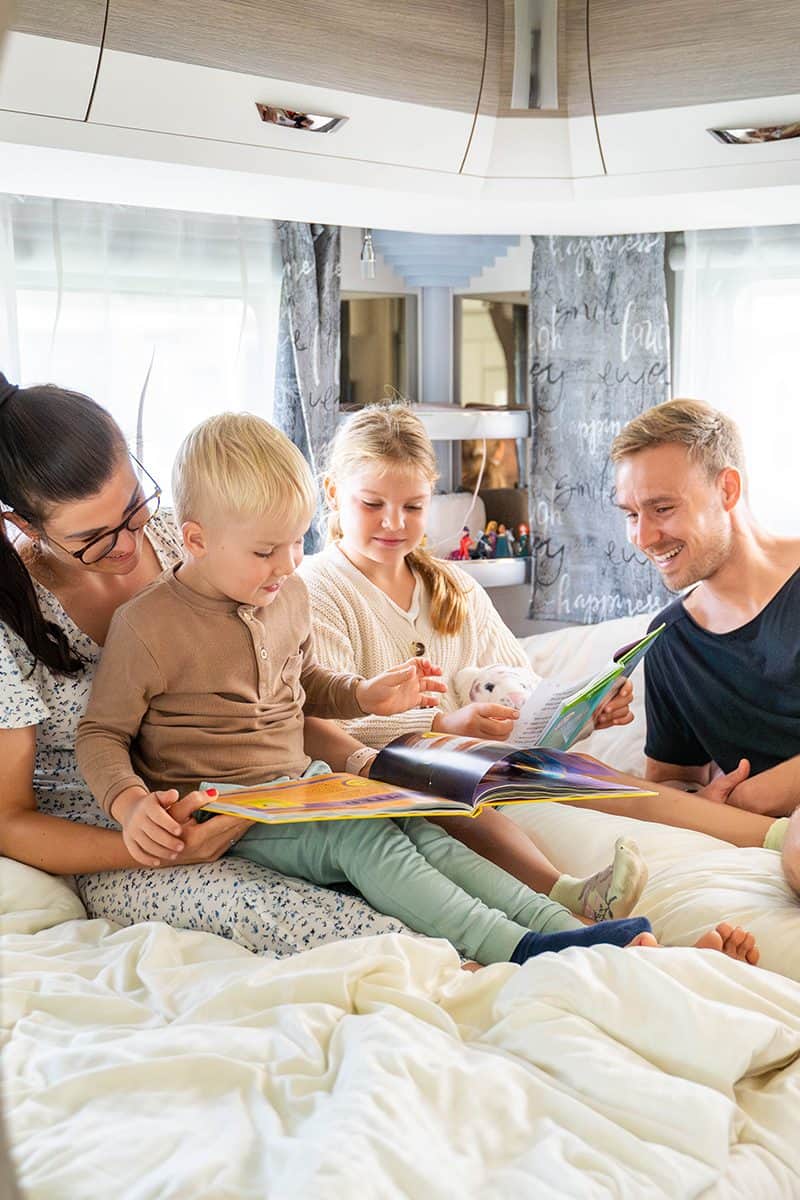 Familie sitzt vor einem Mietwohnwagen mit festem Vorzelt