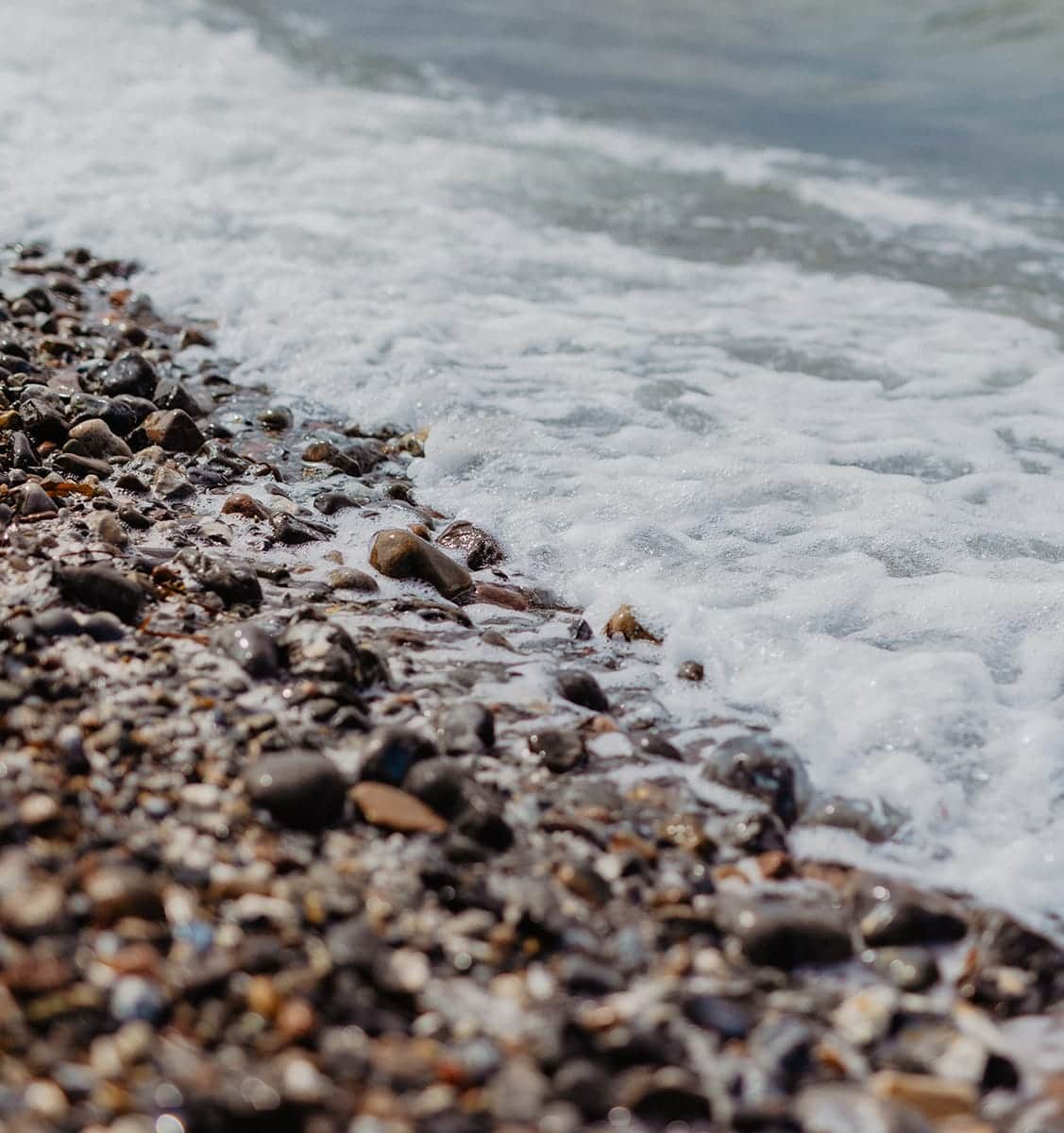 Auslaufende Welle über den Steinen am Naturstrand